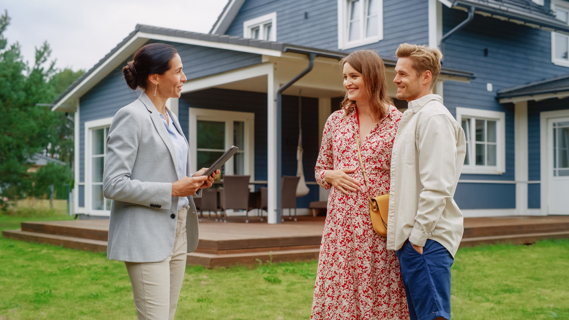 Young Couple Visiting a Potential New Home Property with Professional Real Estate Agent. Female real estate agent Showing the House to Future Homeowners. Focus on For Sale Sign.